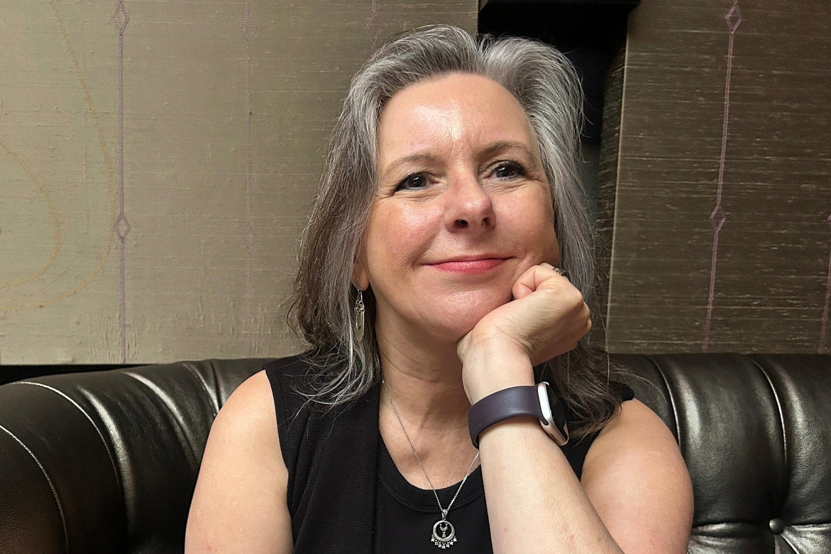 A woman with gray hair sitting in a black leather booth at a restaurant, wearing a black sleeveless top and resting her chin on her hand. 