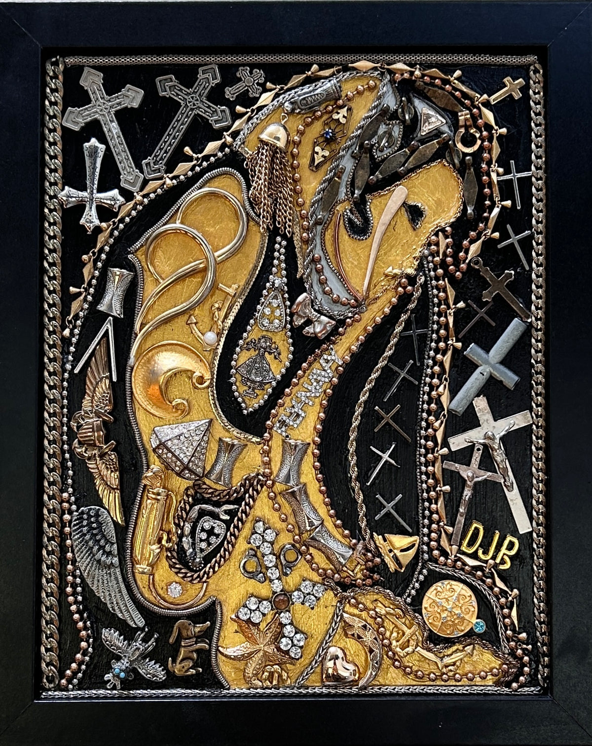 An intricate mixed-media religious artwork featuring a golden and silver-tone horned figure, draped with chains and surrounded by crosses, beads, and ornate metallic details on a black background.
